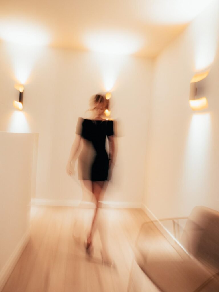 Vervagend silhouet van Fenna Timmermans die door warm verlichte gang loopt.